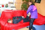 Leonie tied and gagged by Stella on a sofa both wearing sexy shiny nylon rainwear (Pics)