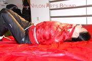 Lucy tied, gagged and hooded on a bed wearing a sexy black shiny nylon pants and a red down jacket (Pics)