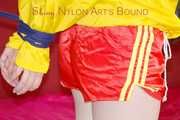 ***LUCIE*** wearing red/yellow shiny nylon shorts and a yellow shiny nylon rain jacket being bound on a sofa with ropes and a ball gag (Pics)