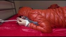 Mara tied and gagged on bed wearing a sexy orange shiny down jacket and a orange rain pants (Video)