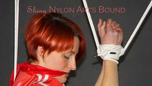 Sonja wearing a black rain pants and a red shiny nylon rain jacket tied and gagged with ropes overhead (Pics)