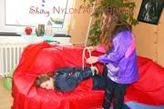 Leonie tied and gagged by Stella on a sofa both wearing sexy shiny nylon rainwear (Pics)