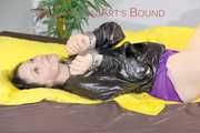 LUCY tied and gagged on a pillory in a bed wearing a supersexy selfmade purple shiny nylon shorts and a black rain jacket (Pics)