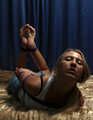 Barefoot Nancy in white tank-top and jeans shorts, hogtied with violet hemp rope, wiggles on the bed