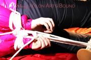 Mara tied, gagged and hooded on bed wearing a black rain pants and a pink down jacket (Pics)