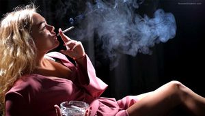 Blonde girl is smoking a cigarette is the dark room