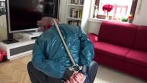 Mara tied and gagged on a chair with a bar wearing a sexy blue shiny nylon rain pants and a green rain jacket (Video)