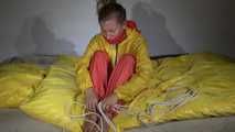 Watching Sandra  wearing an orange shiny nylon rain pants and a yellow shiny nylon rain jacket being tied and gagged on a bed with ropes and a clothgag (Video)