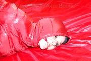Lucy tied, gagged and hooded on a bed wearing a sexy black shiny nylon pants and a red down jacket (Pics)