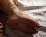 Topless barefoot Cheryl, lying under a blanket, is getting herself gagged and hogtied by a man
