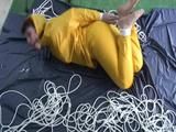 Archive girl tied and gagged on bed wearing a shiny yellow rainwear (Video)