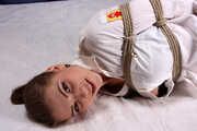 Barefoot Lisa in white shirt and jeans shorts, hogtied with hemp rope, wiggles and rolls on the bed