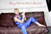 PIA tied and gagged with a pillory on a sofa wearing a sexy blue really shiny nylon rain bib overall (Pics)