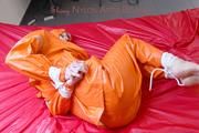 Pia tied and gagged in bed in a orange rainsuit and a red gag (Pics)