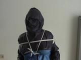 An archive girl tied, gagged and hooded two times on a sofa and chair wearing a shiny blue rainwear (Video)