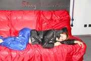Sonja wearing a blue shiny nylon raver pants and a black down jacket posing and lollingn on the sofa (Pics)