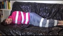 Mara tied and gagged with tape on a blue sofa wearing a supersexy pink/grey rainwear combination (Video)