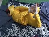 Archive girl tied and gagged on bed wearing a shiny yellow rainwear (Video)