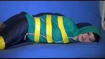 Mara tied, gagged and hooded with tape on a blue sofa wearing an blue/green rain combination (Video)