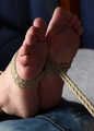 Topless barefoot ballgagged Carolyn in jeans shorts, hogtied with hemp rope, wiggles and rolls on the bed