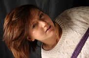 Barefoot Gwen in sweater and short skirt, suspended sideways with violet hemp rope, dangles in the air