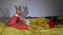Watching Sandra  wearing an orange shiny nylon rain pants and a yellow shiny nylon rain jacket being tied and gagged on a bed with ropes and a clothgag (Video)
