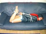 Leonie tied, gagged and hooded sitting on a sofa wearing a sexy shiny nylon shorts and a rain jacket (Pics)
