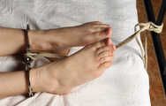 Topless barefoot Cheryl is being gagged and cuffed to the bed on-screen
