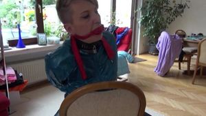 Mara tied and gagged on a chair with a bar wearing a sexy blue shiny nylon rain pants and a green rain jacket (Video)