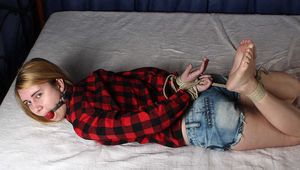 Ballgagged barefoot Carolyn, hogtied with hemp rope, wiggles on the bed
