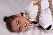 Barefoot Lisa in white shirt and jeans shorts, hogtied with hemp rope, wiggles and rolls on the bed