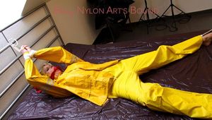 Pia tied and gagged in bed in a yellow rainsuit and a red gag