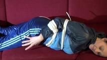 Lucy tied and gagged on a red sofa wearing a supersexy blue shiny nylon pants and a blue rain jacket (Video)