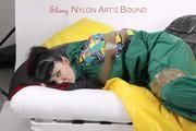 Jill tied and gagged with tape on bed wearing a shiny green nylon rainsuit (Pics)