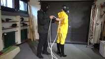See Lady M, bound in shiny yellow Rainsuit, wearing a latex Mask and a Gasmask