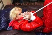 Pia tied and gagged on bed wearing a shiny red rain pants and a shiny red/purple down jacket (Pics)