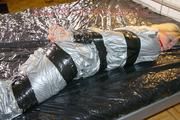 Pia tied and gagged with tape on a bed wearing a sexy silver rainwear combination (Pics) 