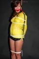 Alina tied and gagged to a pole in nylon shorts and yellow cagoule