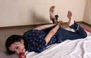Emily in violet short-sleeve and jeans, hog-cuffed with steel cuffs, wiggles on the floor