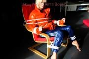 Pia tied and gagged on a chair wearing a shiny orange down jacket and a shiny blue rain pants (Pics)