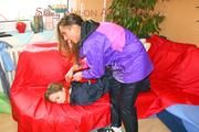 Leonie tied and gagged by Stella on a sofa both wearing sexy shiny nylon rainwear (Pics)
