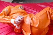 Pia tied and gagged in bed in a orange rainsuit and a red gag (Pics)