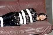 Mara wearing a sexy shiny black rian pants and a sexy shiny black rain jacket tied and gagged with tape and cloth gag on a sofa (Pics)