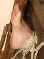 Topless barefoot Florence, lying on the floor with her hands tied in front of her and with her feet locked in stocks, is tickled by a man