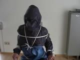 An archive girl tied, gagged and hooded two times on a sofa and chair wearing a shiny blue rainwear (Video)