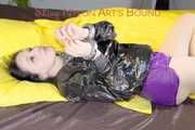 LUCY tied and gagged on a pillory in a bed wearing a supersexy selfmade purple shiny nylon shorts and a black rain jacket (Pics)