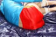 Pia tied and gagged on a bed wearing a shiny red nylon shorts and a blue rain jacket (Pics)