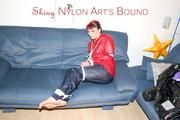 Jill tied, gagged and hooded infront of a sofa wearing a darkblue rain pants and a red rain jacket (Pics)