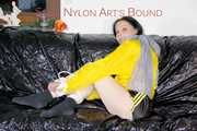 LUCY tied and gagged with ropes and a ballgag on a sofa wearing a sexy black/yellow shiny nylon shorts and a yellow rain jacket (Pics)