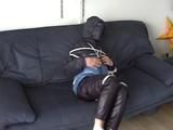 An archive girl tied, gagged and hooded two times on a sofa and chair wearing a shiny blue rainwear (Video)